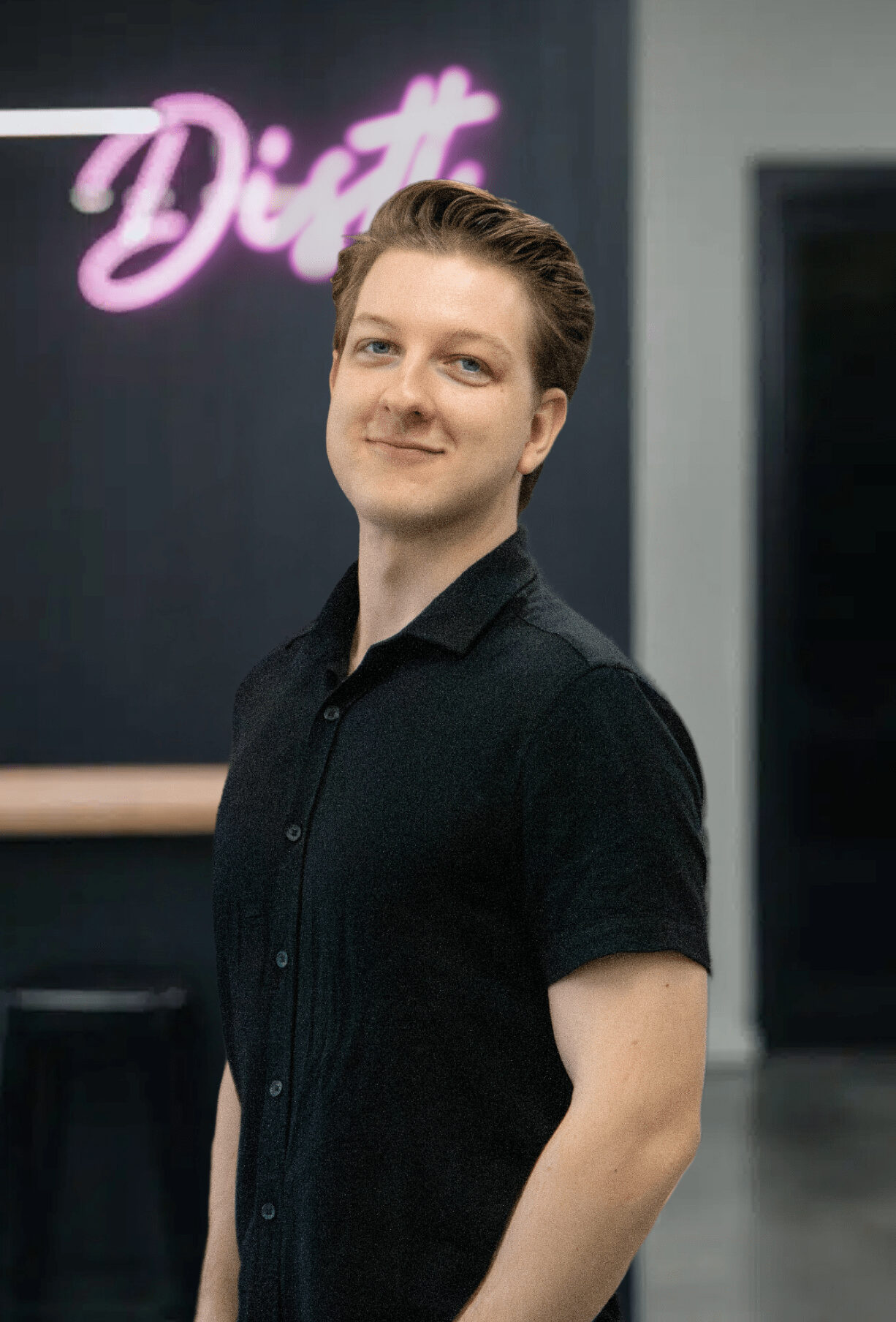 DSLR Portrait Image of Jakeb Munn who is an SEO specialist in Perth. He is smirking and has short blonde styled hair and is wearing a short sleeve black button up shirt.